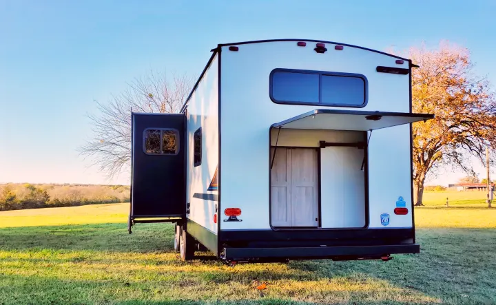 Spacious rv rental travel trailer with open rear ramp and slide-out extended in a serene outdoor setting, perfect for camping.. Coachmen Northern Spirit 2024