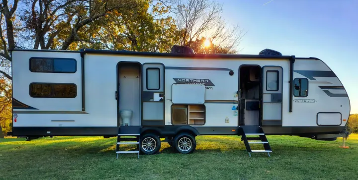 This RV rental showcases its extended slide-out, open doors, and outdoor amenities like a toilet and storage, perfect for camping.. Coachmen Northern Spirit 2024