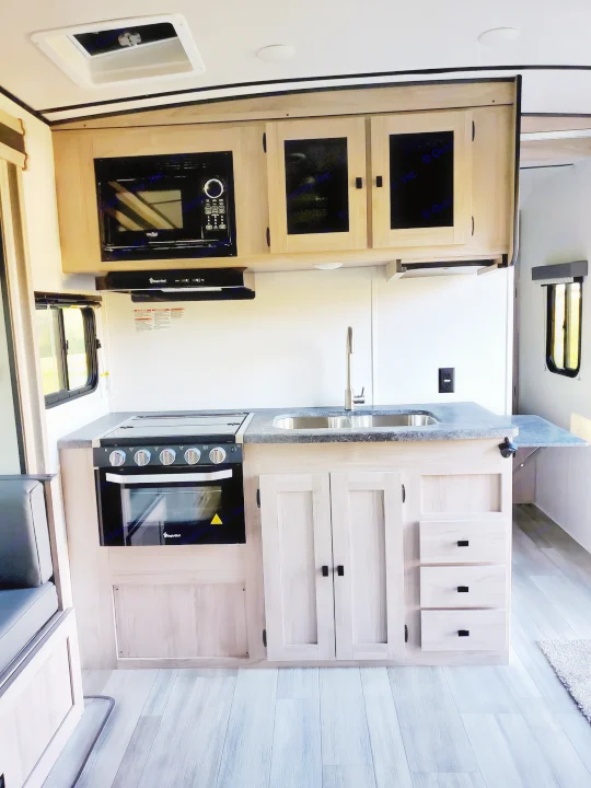 Modern RV rental kitchen with microwave, oven, sink, and light wood cabinets, perfect for travelers.. Coachmen Northern Spirit 2024