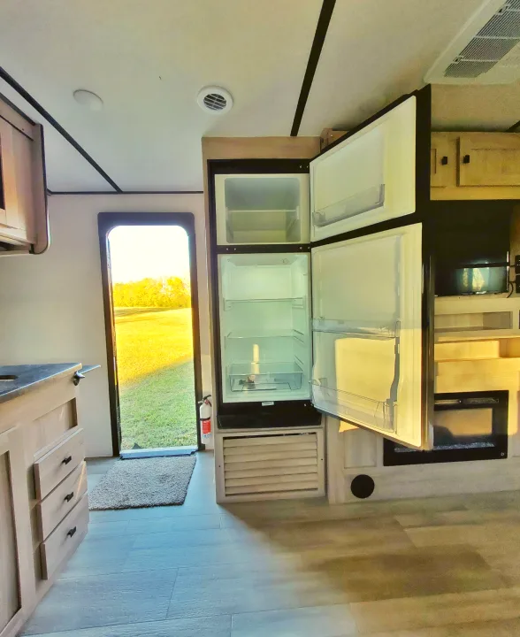 Bright RV rental interior features a clean kitchen with open refrigerator, a cozy fireplace, and an inviting outdoor view.. Coachmen Northern Spirit 2024