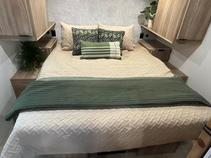Cozy RV rental bedroom featuring a comfy bed with green & cream bedding, patterned pillows, and modern wood cabinets.. Winnebago Access 26 RL 2024