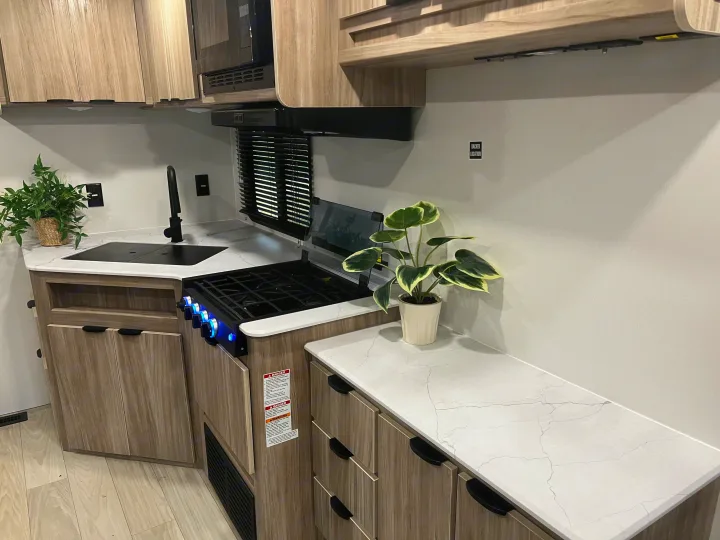 Modern RV rental kitchen with sink, stove, and microwave, featuring light wood cabinets & marbled countertops.. Winnebago Access 26 RL 2024