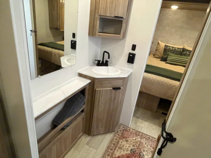 Compact RV rental living space showing a bathroom vanity with a black faucet and a mirrored view into the bedroom.. Winnebago Access 26 RL 2024