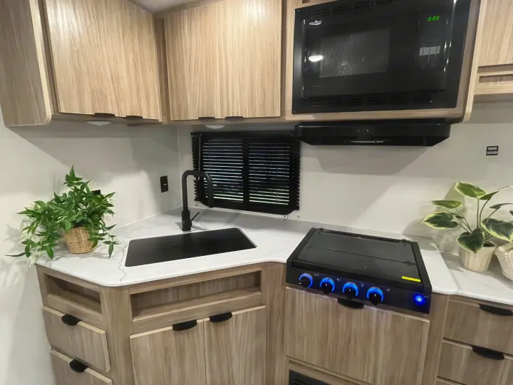Compact RV rental kitchen features a microwave, sink, and stovetop. Modern design with light wood cabinets.. Winnebago Access 26 RL 2024