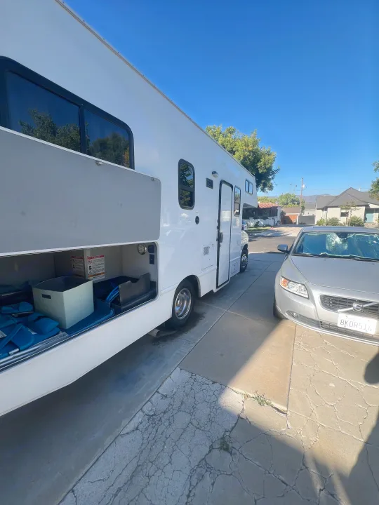 Sunny day RV rental parked with storage open, next to a silver Volvo. Perfect for trips!. Thor Majestic 2019