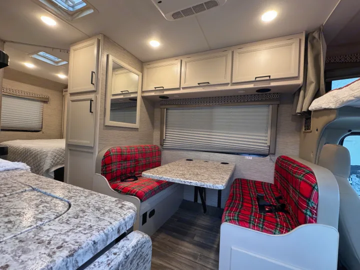 Cozy RV rental interior with a vibrant red plaid dinette, compact kitchen, and inviting bedroom area.. Thor Freedom Elite 2022