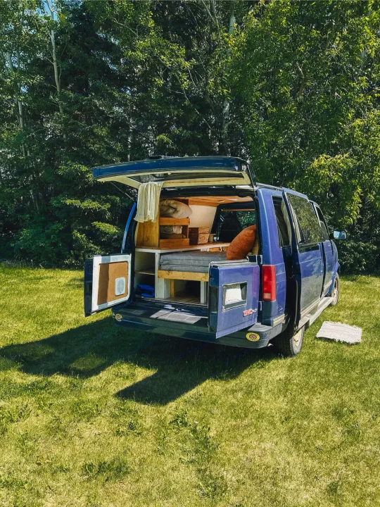 Blue camper van with open back, showing a cozy, custom-built interior. Perfect for your next RV rental!. Gmc Safari 1996