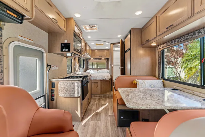 Discover this well-appointed RV rental interior: kitchen, dinette, and cozy bedroom, all with light wood finishes.. Thor Four Winds 2019
