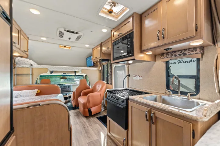 Modern RV rental interior featuring a well-equipped kitchen, dining booth, and overhead bunk.. Thor Four Winds 2019
