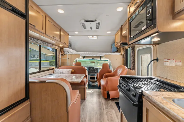 Spacious RV rental interior featuring a modern kitchen, dinette, cab-over bunk, and driving area with light wood finishes.. Thor Four Winds 2019