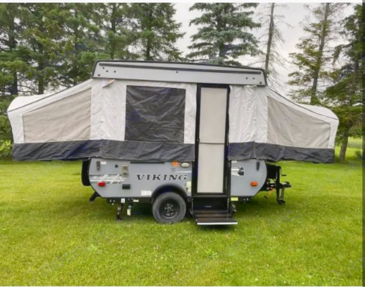 A grey pop-up camper, ideal for an RV rental, is fully set up on a green lawn surrounded by trees.. Coachmen epic 1906 2019