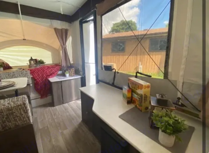 Inside a comfortable RV rental: dining booth with red blanket, kitchen counter with decor, and a large view window.. Coachmen epic 1906 2019