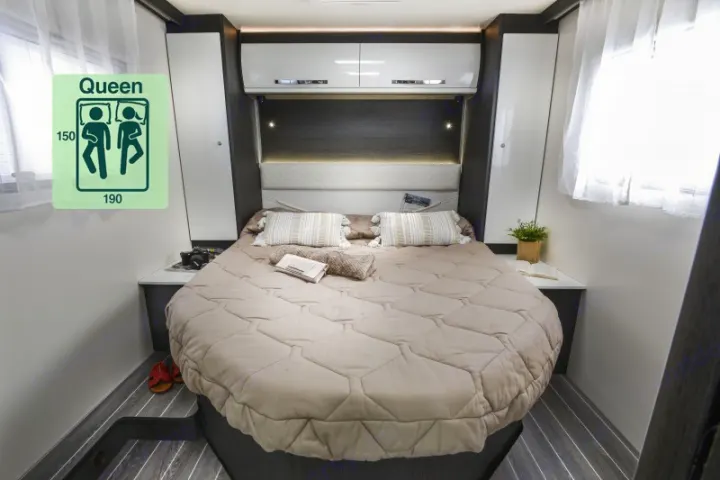 Queen bed in a modern RV rental bedroom featuring overhead cabinets, ambient lighting, and bedside tables.. Roller Team 696 2024