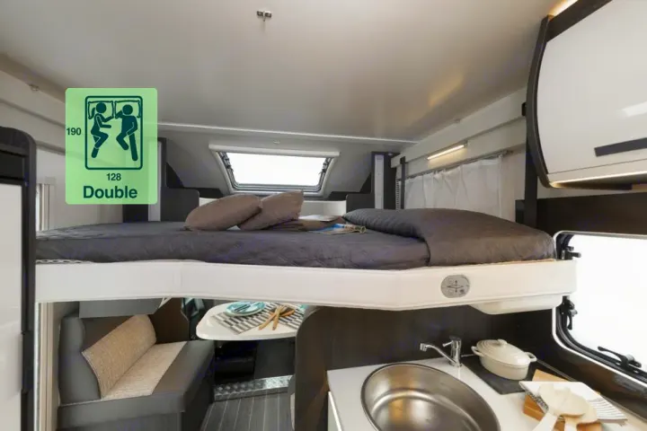 This RV rental shows a clever interior: an elevated double bed over a compact kitchen and dining area, maximizing space.. Roller Team 696 2024