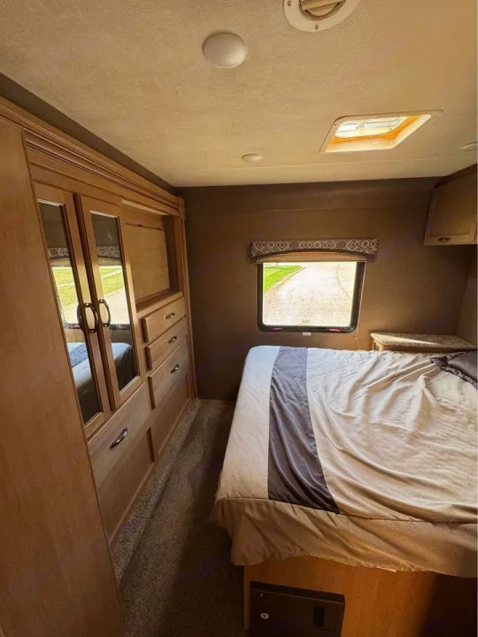 Cozy RV rental bedroom featuring a comfortable bed, large mirrored wardrobe, and a window with an outdoor view.. Thor Motor Coach Chateau 2019