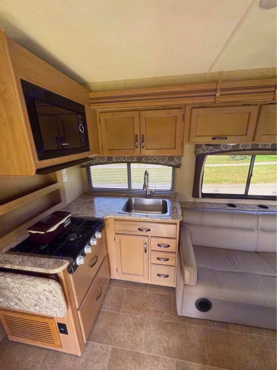 Compact RV rental kitchen with stove, sink, microwave, and ample cabinets. A comfy sofa offers relaxation in this functional RV interior.. Thor Motor Coach Chateau 2019