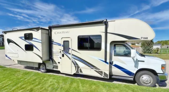 This Thor Chateau RV rental, a spacious motorhome perfect for travel, is parked on grass under a clear blue sky.. Thor Motor Coach Chateau 2019