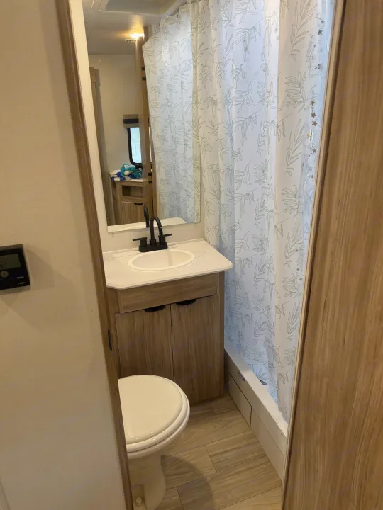 Clean RV rental bathroom with a modern sink, vanity, toilet, and shower featuring a white curtain with green leaf patterns.. Winnebago Access 2024