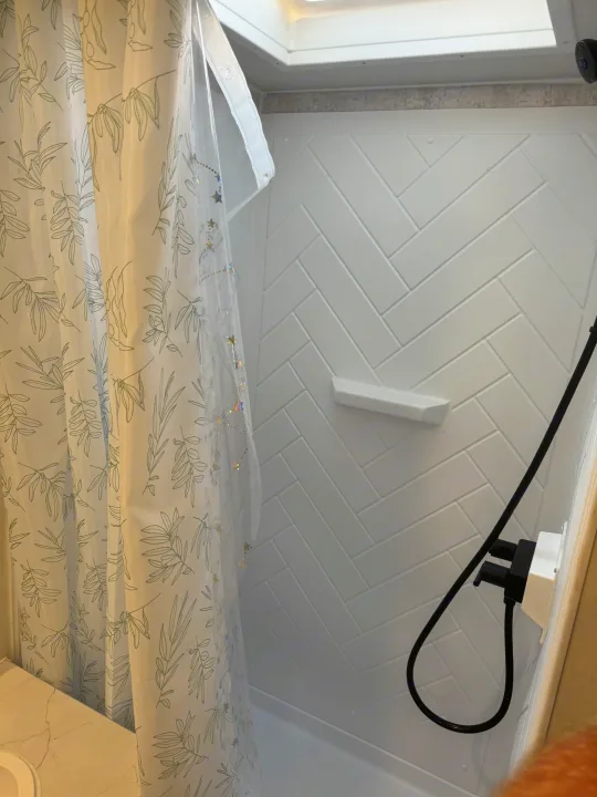 Step inside this modern RV rental shower featuring stylish herringbone walls, a skylight, and leafy curtain. Ready for your adventure!. Winnebago Access 2024