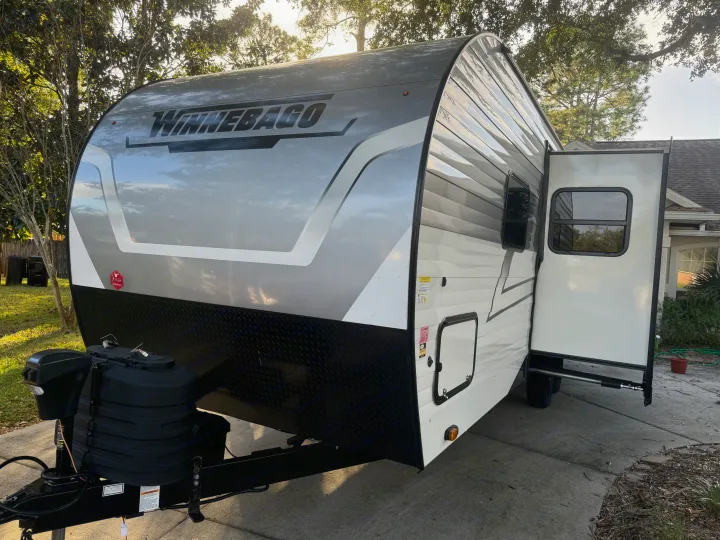 Winnebago travel trailer rv rental, white and gray with open door, parked on a driveway. Ready for adventure.. Winnebago Access 2024