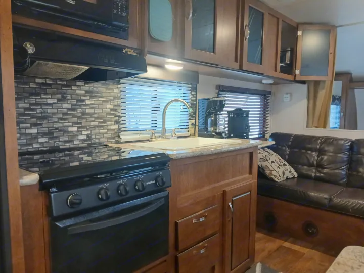 Inside an RV rental: a modern kitchen with a stove, microwave, and sink, next to a comfy brown sofa.. Forest River Salem Cruise Lite 2018