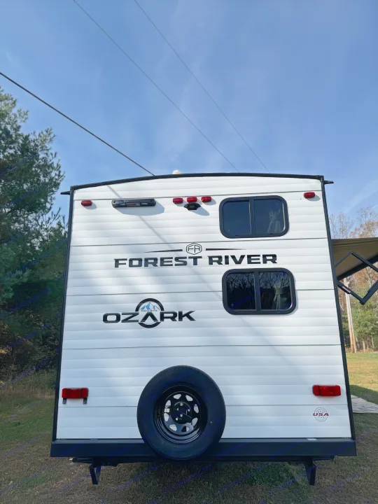 White Forest River Ozark travel trailer, perfect for your next rv rental adventure. Shows rear with windows, tail lights, and spare tire.. Forest River Ozark 2025