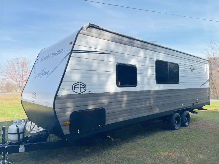 Side view of a modern Forest River Ozark travel trailer rv rental, gray and black, parked on green grass under a blue sky.. Forest River Ozark 2025