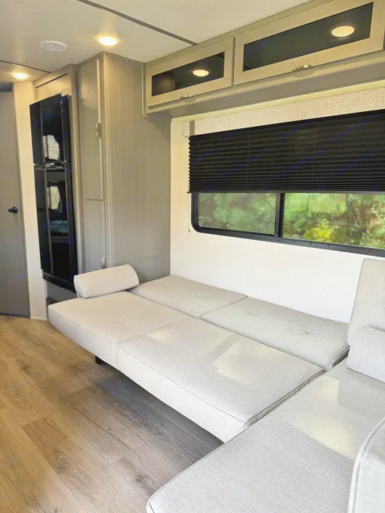 RV rental: Modern interior with a light grey sectional sofa-bed, wood cabinets, and a window view of trees.. Forest River Ozark 2025