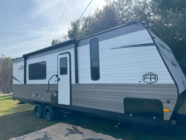 White and gray Forest River Ozark travel trailer (RV rental) parked on grass, ideal for outdoor adventures.. Forest River Ozark 2025