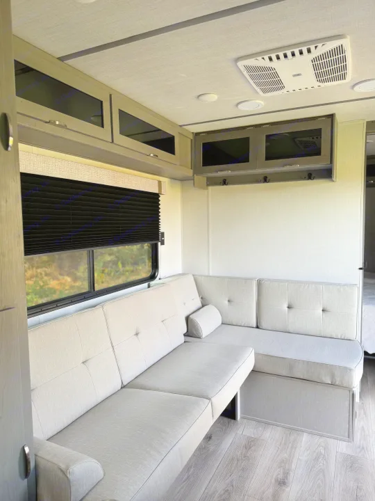 Spacious rv rental interior: L-shaped sofa, window, overhead cabinets, and AC unit for comfort on the road.. Forest River Ozark 2025