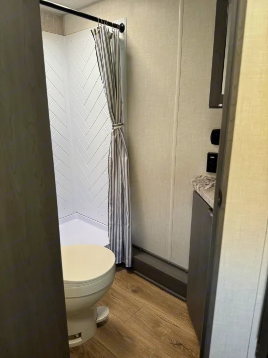 Modern RV rental bathroom featuring a compact shower with herringbone walls, toilet, and a small vanity.. Forest River Ozark 2025
