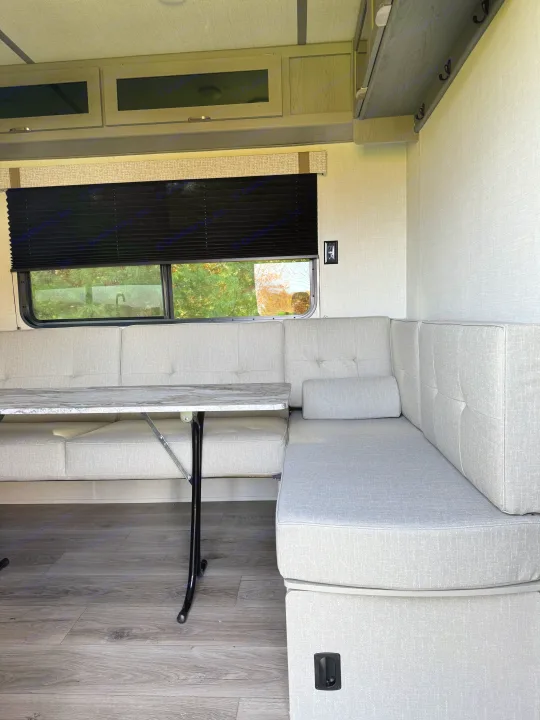 Spacious RV rental dinette with cozy light-gray seating, faux marble table, and overhead storage. Enjoy travel comfort.. Forest River Ozark 2025
