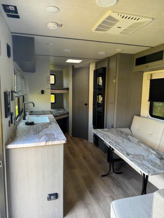 Bright and modern rv rental interior featuring a kitchen with counter and sink, a dinette, and cozy bunk beds.. Forest River Ozark 2025