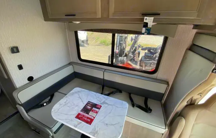 Inside an RV rental: a modern dinette with light and dark gray benches, a white marble-look table, and a large window.. COACHMEN FREELANDER 21RS 2023