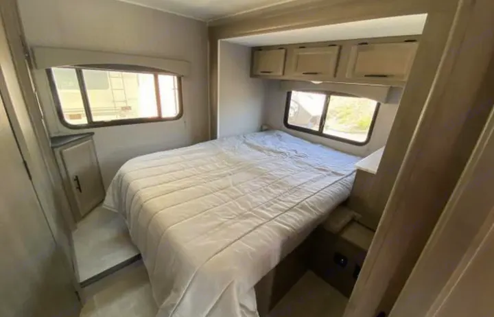 Cozy RV rental bedroom with a comfortable bed, side windows, and overhead storage cabinets.. COACHMEN FREELANDER 21RS 2023