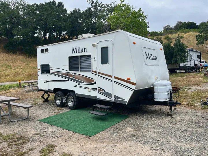 White Milan rv rental travel trailer set up in a rustic campsite with picnic tables and natural surroundings.. Eclipse Recreational Vehicles Milan 2011