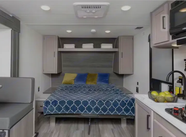 Modern RV rental interior: a comfy bed, overhead storage, kitchen with sink, and dinette. Ideal for travel & camping.. Keystone RV Hideout Sport 2024