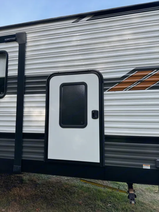 RV rental side with white door, ribbed siding, and graphic details. Stabilizer visible below.. Forest River Wildwood 2021