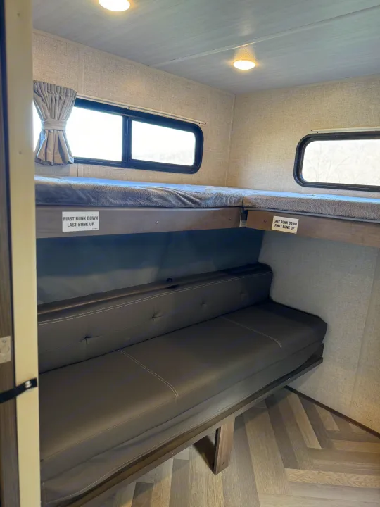 RV rental interior featuring flexible bunk beds above a sofa, ideal for sleeping and lounging in this compact space.. Forest River Wildwood 2021