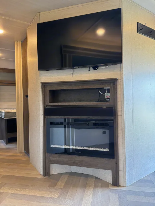 RV rental living space with entertainment center, including TV, Furrion soundbar, and electric fireplace, plus herringbone flooring.. Forest River Wildwood 2021
