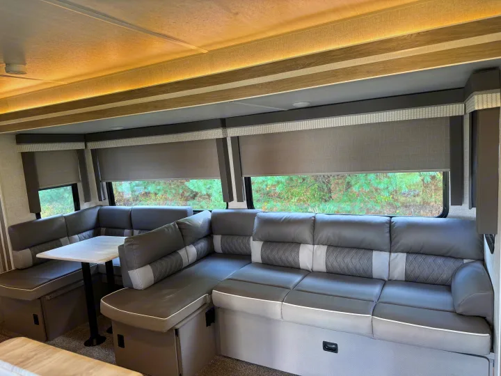 Modern RV rental interior: spacious gray dinette/sofa, windows with blinds, and cozy accent lighting for travel comfort.. Forest River Wildwood 2021