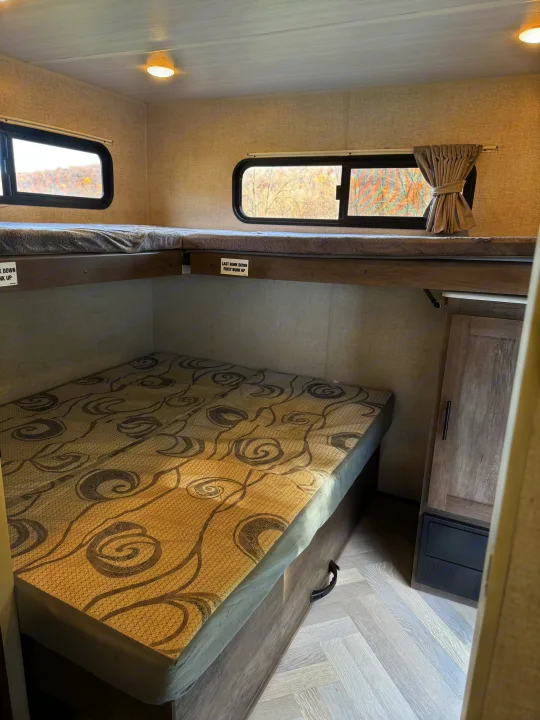 RV rental: Interior of a camper showing a lower patterned mattress, an upper bed with gray blanket, and windows.. Forest River Wildwood 2021