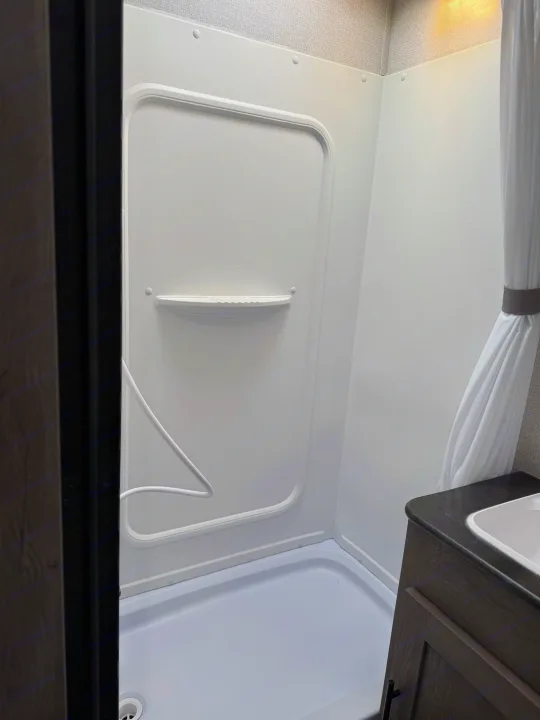 Compact RV rental bathroom with a white shower stall, small vanity, and sink, highlighting efficient space design.. Keystone RV Springdale 2021