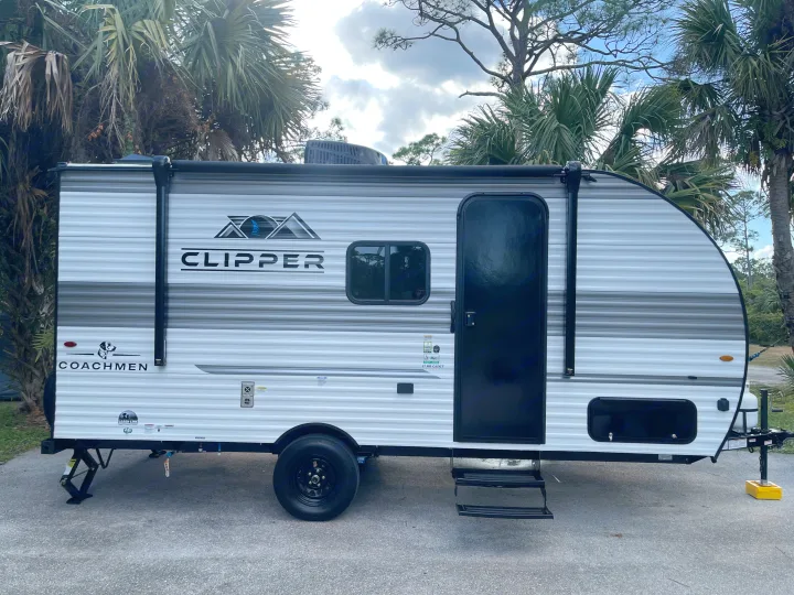 Side profile of a white Coachmen Clipper travel trailer, ready for rv rental, parked among trees.. Coachmen Clipper Cadet 17CBH 2025