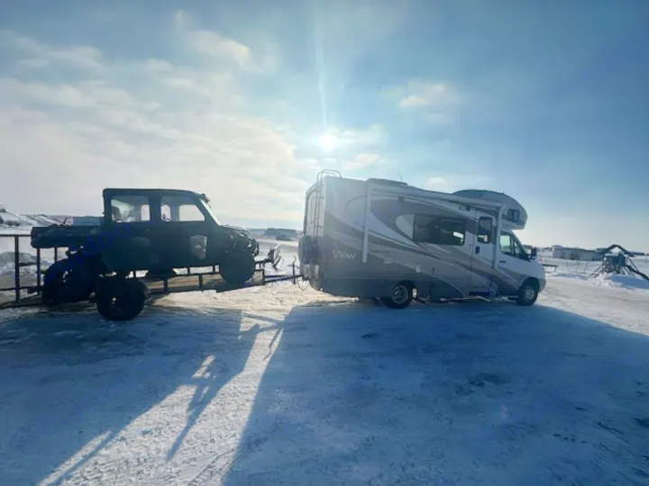 RV rental setup: motorhome towing a utility vehicle on a trailer in bright, snowy winter conditions.. Winnebago View 2011
