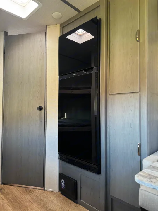 This modern RV rental showcases a sleek black Furrion refrigerator, light wood cabinets, and a clean, functional interior.. Forest River Ozark 2025