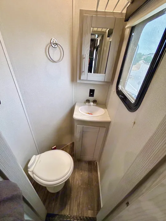 RV rental's compact bathroom: white toilet, sink with vanity, mirrored cabinet, and a view from the window.. Keystone Fuzion 2022