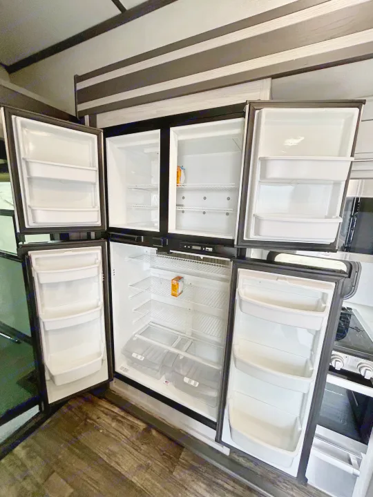 This spacious RV rental refrigerator and freezer, completely empty with doors open, showcases its clean shelves and bins.. Keystone Fuzion 2022