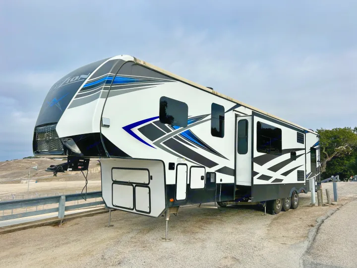Large, modern 'VOLITION' fifth-wheel RV, white with black and blue graphics, perfect as an rv rental for your next trip.. Keystone Fuzion 2022