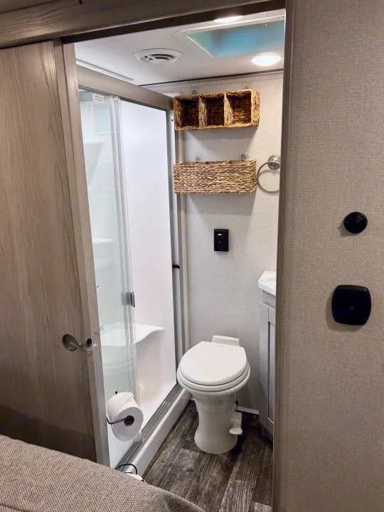 Explore this RV rental's compact bathroom with a bright shower, toilet, sink vanity, and woven storage baskets. Practical and stylish.. Keystone Fuzion 2022